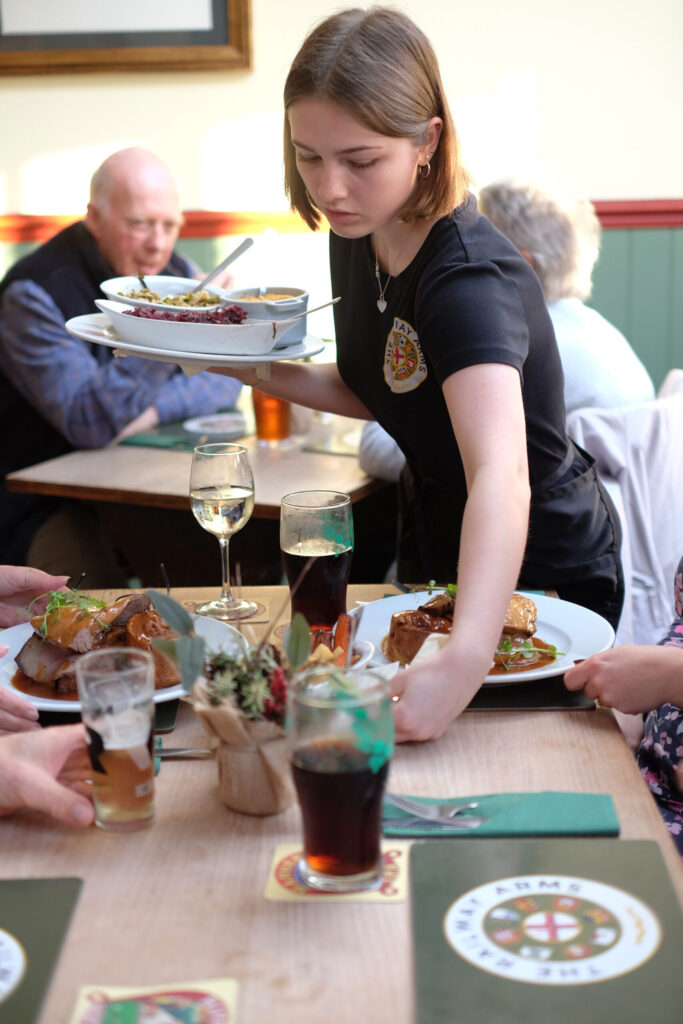 People being served a Sunday country roast in a pub by a young girl whilst drinking beer